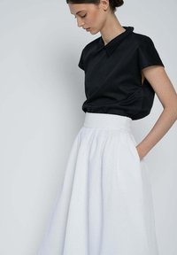 Black short-sleeve blouse with a collar paired with a white textured, high-waisted skirt. The skirt features side pockets.