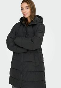 Melna pūkā pudelīte ar kapuci, ar rāvējslēdzēja priekšpusi, lieliem kvadrātiem un sānu kabatām. Izgatavota no viegla, ūdensnecaurlaidīga materiāla.