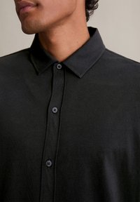 Čierna košeľa s golierom vyrobená z jemného materiálu, s tmavými gombíkmi a hladkým povrchom, ktorý vykazuje čistý a minimalistický dizajn.