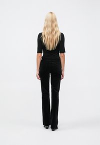 Fekete kordbársony, bővülő szárú nadrág sima textúrával. Bokáig érő magassarkúba tűrve, karcsúsított fekete rövid ujjú felsővel párosítva.