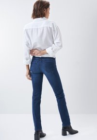 Jeans de mezclilla azul con un corte ajustado, combinados con una camisa blanca de botones. Los jeans cuentan con bolsillos y detalles de costura sutiles. Botines negros con tacón.