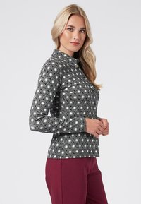 Camicia nera con motivo circolare bianco, maniche lunghe, design colletto e chiusura con bottone al collo. Indossata con pantaloni bordeaux.
