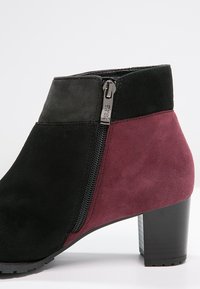 Stivaletto in suede nero e bordeaux con zip laterale, punta arrotondata e tacco a blocco. Presenta sezioni di materiale contrastante per un tocco di dettaglio in più.