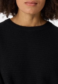 Pull en maille noire avec un design côtelé classique et un col rond, fabriqué dans un matériau en tricot doux.