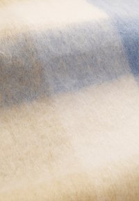 Mykete, teksturerte stoffer med et lyst beige og blå rutemønster, som fremkaller en varm og koselig atmosfære. Ideell for tepper eller bekledning.