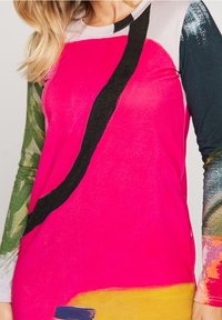 Top de manga larga con cuerpo de color rosa brillante, una franja diagonal negra y mangas texturizadas con patrón verde. Presenta un bloque de color abstracto.