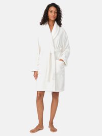 Biały szlafrok wykonany z miękkiej tkaniny, posiadający kołnierz szalowy, boczne kieszenie oraz pasek do wiązania, o długości do połowy łydki. Gładka tekstura.