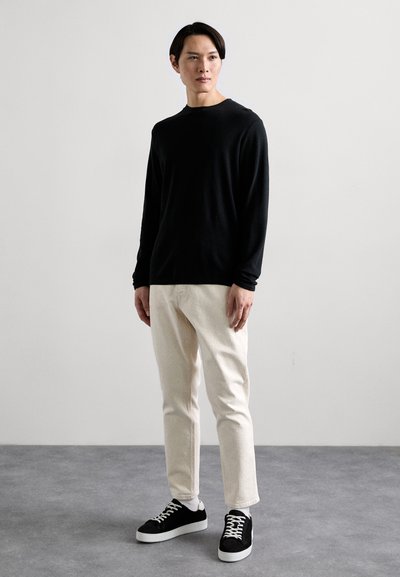 Schwarzes Langarmhemd aus weichem Stoff, kombiniert mit hellen Jeans und schwarzen Sneakers mit weißen Sohlen und Schnürsenkeln.