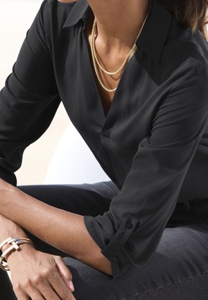 Černá halenka s dlouhým rukávem, výstřihem do V a zapínáním na knoflíky na manžetách, vyrobená z hladké látky. Nositelná s vrstvenými zlatými náhrdelníky a náramkem.