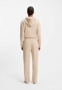 Beżowa bluza z kapturem i dopasowane dresy wykonane z miękkiego materiału. Bluza ma sznurek do regulacji kaptura i kieszeń kangurkę; dresy posiadają elastyczną talię.