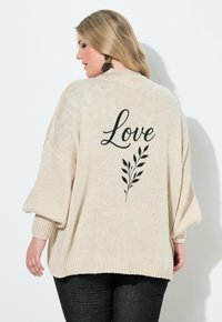 Maglione oversize color crema con orlo e polsini a coste, caratterizzato da una grafica nera con la scritta "Love" e un disegno di foglie sulla schiena.