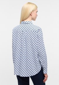 Bageste udsigt af en langærmet skjorte i hvid med et blåt geometrisk mønster, der har en klassisk krave og en buet kant.