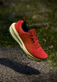Red running shoe with a textured mesh upper, yellow accents, and a cushioned sole featuring a light blue outsole. Lightweight design.