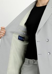 Jasnoszara marynarka w kolorze, o textured powierzchni, z kontrastową beżową podszewką i kieszenią z metką logo wewnątrz.
