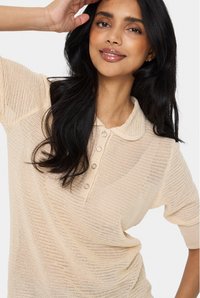 Polo top lavorato a maglia crema con colletto a costine, chiusura a cinque bottoni e maniche corte con vestibilità ampia e motivo testurizzato.