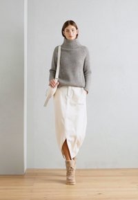 Suéter gris de cuello alto acanalado combinado con una falda midi crema que presenta una abertura frontal. Botines tobilleros de color marrón y un bolso bandolera blanco completan el look.