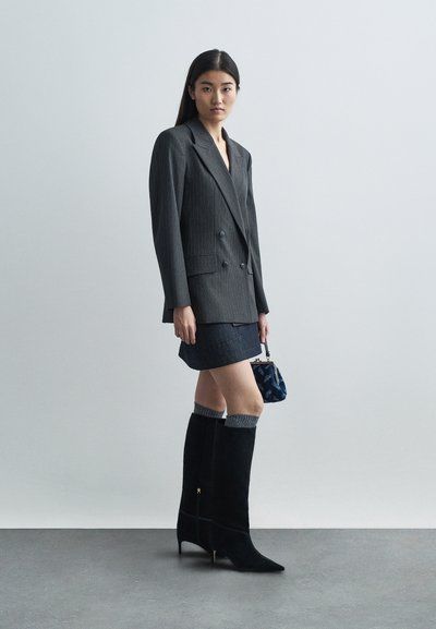 Γκρίζο σακάκι με ρίγες, διπλό κουμπί, τζιν φούστα, μαύρες σουέντ μπότες μέχρι το γόνατο με γκρι ριγέ μανσέτες και τσάντα σε μπλε σχέδιο.