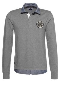 Graues Langarm-Polohemd mit einem Kragen aus Chambray, das ein rundes Logo-Patch auf der linken Brust und einen geraden Saum hat.