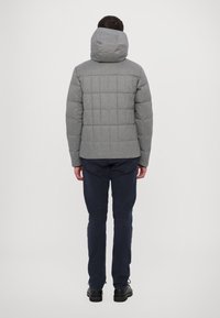 Grå vadderad jacka med huva, med en kviltad design. Slät textur och en snug passform, ihopparad med mörkblå byxor och svarta skor.