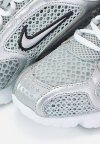 Gros plan sur des baskets Nike argentées et blanches avec tissu en mesh et logo Nike swoosh contour noir sur le côté.