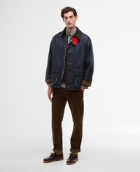 Casaco impermeável azul-marinho com colarinho de corduroy, detalhes em vermelho, dois bolsos frontais, combinado com calças de corduroy castanhas e sapatos castanhos-escuros.