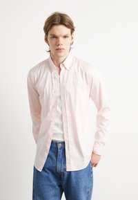 Cămașă butonată în dungi roz deschis, cu guler, având o croială ajustată și cusături vizibile. Purtați cu blugi din denim albastru.