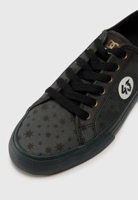 Black canvas sneaker with a textured star pattern, black laces, gold eyelets, and a white logo accenting the side. Rubber sole.