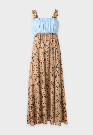 Femme aux longs cheveux foncés portant une robe midi sans manches à imprimé léopard avec un corsage bleu clair et des sandales noires.