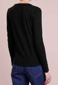 Musta pitkähihaisen paita pehmeästä kankaasta, jossa on yksinkertainen pyöreä kaula-aukko ja tiukka siluetti, yhdistettynä korkea vyötäröinen sinisiin farkkuihin.