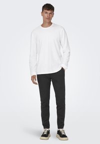 Camiseta blanca de manga larga combinada con pantalones gris oscuro y zapatillas negras con suelas beige. Diseño simple, corte clásico y textura suave.