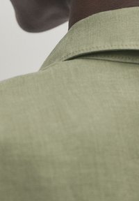 Gros plan sur le cou et l'épaule d'une personne portant un vêtement à col texturé vert clair.