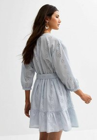 Lichtblauwe jurk met oogjesborduur, driekwartmouwen, een gelaagde zoom en een tailleband voor definitie en silhouet.