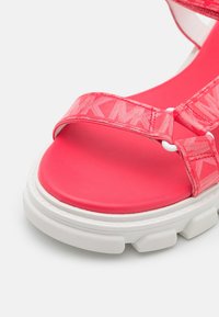 Rosa Sandale mit strukturierten Riemen, gepolstertem Fußbett und einer weißen klobigen Sohle. Verfügt über Logodetails auf den Riemen und eine glatte Oberfläche.