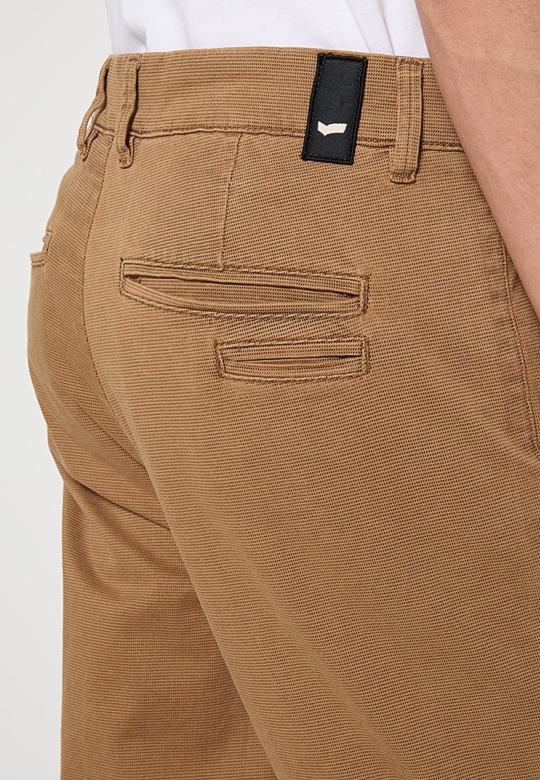 Hosen aus braunem, strukturiertem Stoff mit zwei Gesäßtaschen, einem dezenten Streifenmuster und einem schwarzen Markenschild am Taillenbund.