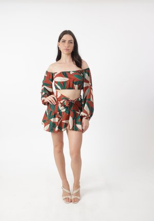 Conjunto de top corto con los hombros al descubierto y falda a juego, con un fondo óxido, patrones de hojas verdes y beige, y un detalle atado en la cintura.