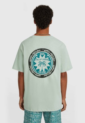 T-shirt en coton vert menthe avec un motif circulaire représentant des palmiers et "California 1952" en turquoise et noir. Manches courtes, coupe décontractée.