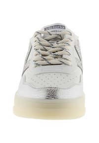 Zapatilla blanca y plateada con cordones beige, puntera perforada y suela gruesa translúcida, vista desde el frente.