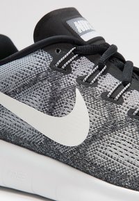 Ingrandimento di una scarpa da corsa Nike in bianco e nero con tessuto a maglia, logo swoosh bianco, lacci neri e suola bianca contrassegnata da "FREE."