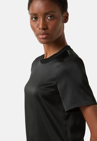 Schwarzes T-Shirt mit kurzen Ärmeln aus glattem Stoff, mit rundem Halsausschnitt und minimalistischem Design. Keine auffälligen Muster oder Akzente.