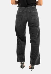 Pantalones vaqueros negros de cintura alta con un ajuste holgado, material de mezclilla, dos bolsillos traseros y un diseño de pierna recta. La tela tiene un ligero desgaste.