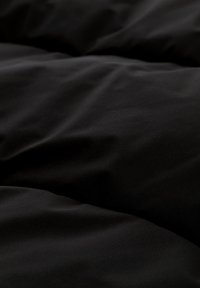 Sort dyneovertræk med en glat, mat tekstur. Stoffet synes blødt og let krøllet, hvilket viser subtile folder og skygger.