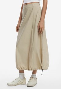 Beige, knee-length skirt with a gathered hem, made from lightweight fabric; features a smooth texture and an elasticized bottom.