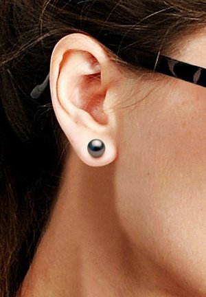 Boucle d'oreille en perle noire en forme ronde, présentant une surface lisse. Présentée sur un teint de peau clair et en vue latérale de l'oreille.