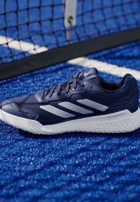 Granatowe buty sportowe z białymi paskami, teksturowana cholewka, wyściółka w podeszwie i logo Cloudfoam+, umieszczone na niebieskiej syntetycznej powierzchni.