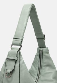 Bolso de mano de cuero verde claro con una correa ancha, forma triangular, textura suave y detalle de cremallera plateada.