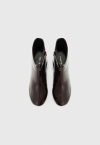 Botas de tobillo burdeos con un acabado brillante, que cuentan con una cremallera lateral y un diseño estrecho y afilado. Textura suave, estilo minimalista.