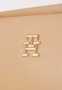 Guldinterlåsade "T" och "H" logotyp på en texturerad beige läderyta av en handväska eller accessoar.
