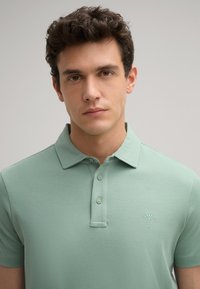 Polo shirt in zachtgroene katoen met een klassieke kraag, drie knoopsluitingen en geborduurd logo op de linkerkant van de borst. Glad van textuur.