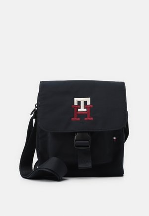 Borsa a tracolla navy realizzata in tessuto con chiusura a pattina, caratterizzata da un logo ricamato in rosso e bianco. Include una tracolla regolabile.