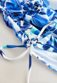 Costum de baie albastru cu model floral, fabrică adunată, accente albe și șnur reglabil. Textură netedă cu modele îndrăznețe și colorate.